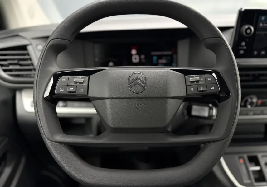 Gros plan sur le volant multifonction noir du Citroën Jumpy 2025 avec commandes intégrées et tableau de bord numérique flou.