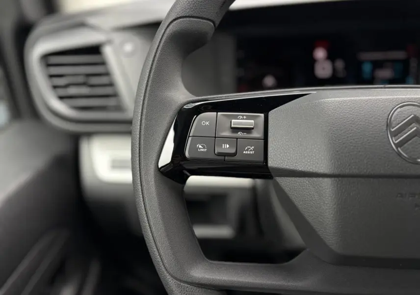 Gros plan sur les commandes au volant noir du Citroën Jumpy 2025, avec logo et tableau de bord flou en arrière-plan.