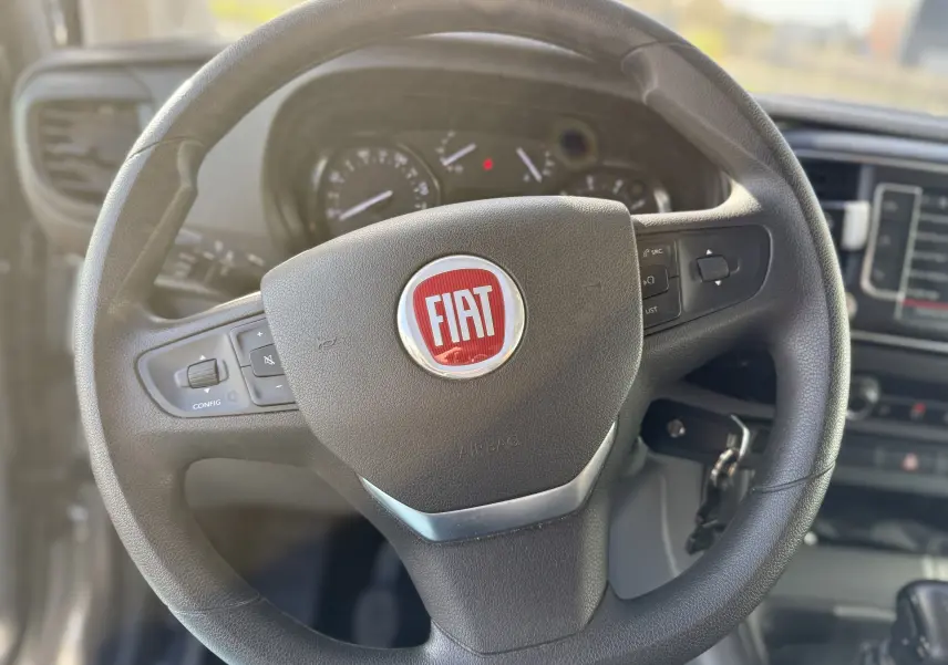Vue rapprochée du volant noir avec logo FIAT rouge du Fiat Scudo Cabine Approfondie gris, tableau de bord en arrière-plan flou.
