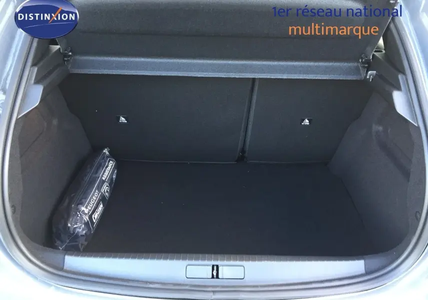 Coffre ouvert d'une Peugeot 208 gris selenium metal, montrant un espace de rangement vide avec une trousse d'assistance sur la gauche.