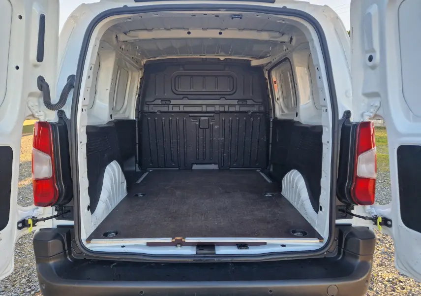 Vue arrière ouverte du Peugeot Partner blanc 2021, montrant l'espace de chargement vide avec plancher en bois et parois noires.