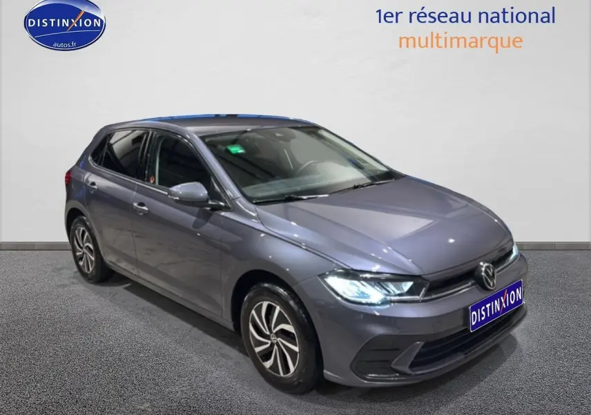 Volkswagen Polo gris cendre vue 3/4 avant droit avec phares allumés et jantes alliage.
