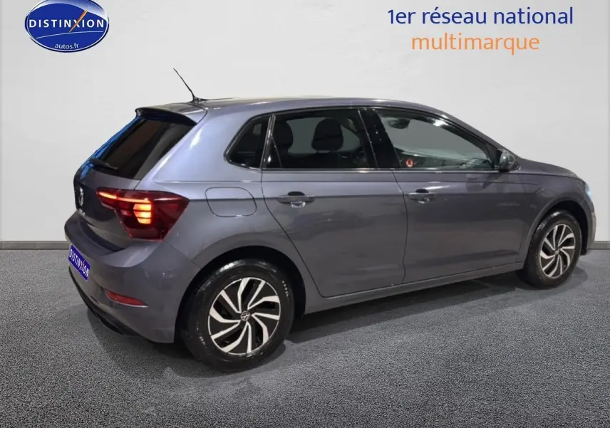 Volkswagen Polo gris cendre vue de profil côté droit avec feux arrière allumés en intérieur showroom.