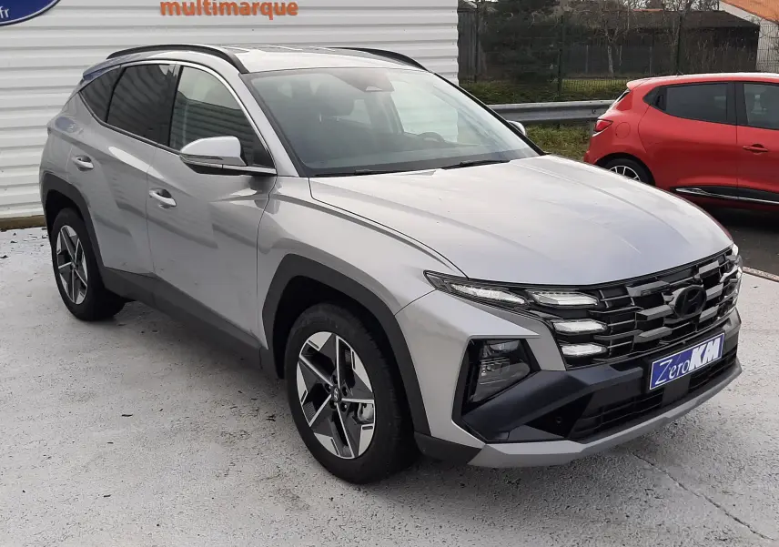 Vue 3/4 avant d'un Hyundai Tucson gris Shimmering Silver 2025, avec calandre noire et jantes bi-ton distinctives.