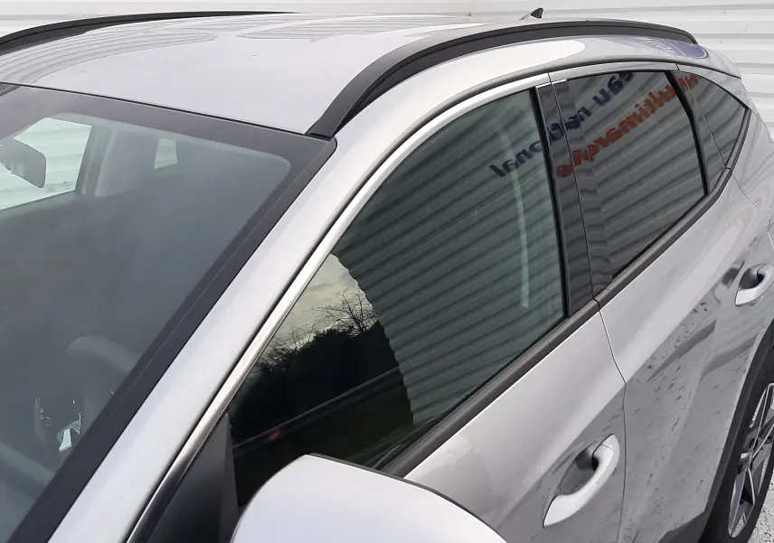 Vue 3/4 avant droit du Hyundai Tucson gris Shimmering Silver 2025, avec rétroviseur et toit ouvrant visibles.