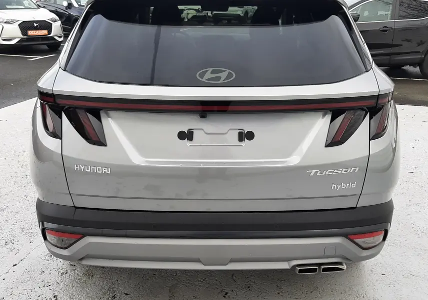 Vue arrière d’un Hyundai Tucson hybride gris Shimmering Silver avec feux arrière en bandeau lumineux et double sortie d’échappement.