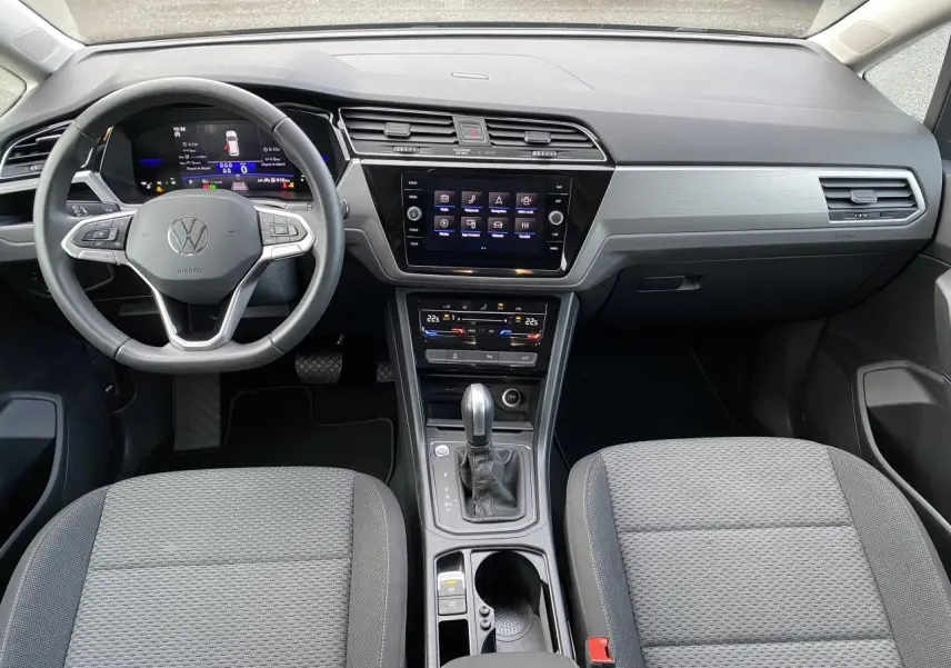 Vue intérieure frontale du tableau de bord et console centrale du Volkswagen Touran 2025 avec volant cuir multifonction et écran tactile.