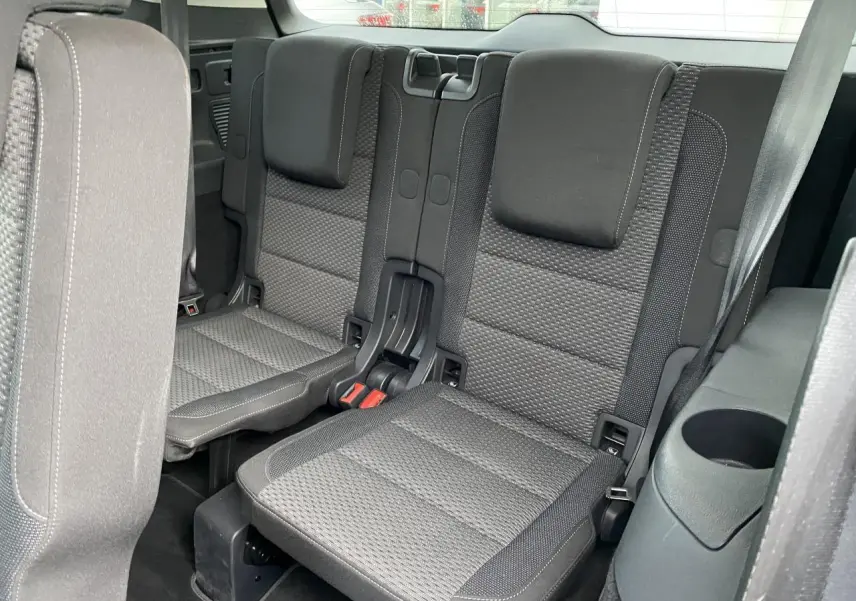 Vue intérieure sur les sièges arrière gris foncé du Volkswagen Touran 2025, avec accoudoir et porte-gobelet intégrés.