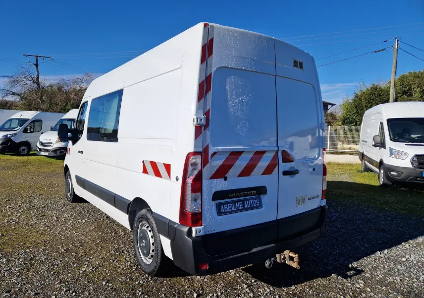 Vue 3/4 arrière droite d’un Renault Master blanc avec marquages réfléchissants rouges et blancs, stationné en extérieur.