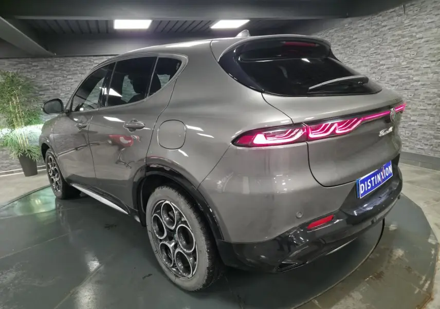 Vue 3/4 arrière droite de l'Alfa Romeo Tonale gris métallisé avec feux arrière LED allumés en intérieur showroom.