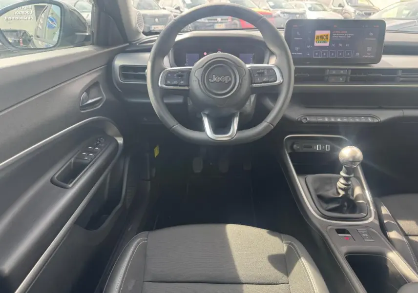 Vue intérieure frontale du poste de conduite du Jeep Avenger gris foncé 2025 avec volant multifonction et boîte manuelle.