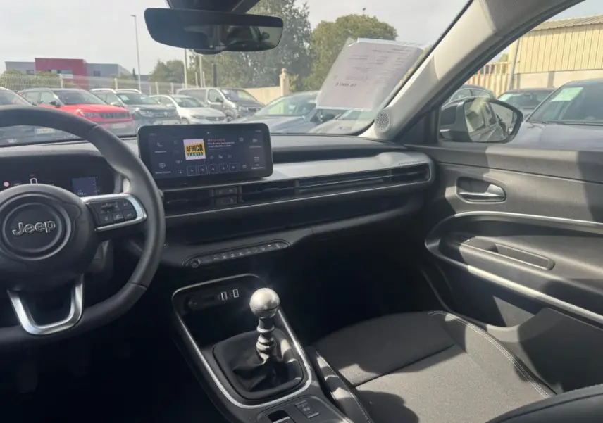 Vue intérieure côté conducteur du Jeep Avenger gris foncé 2025, avec tableau de bord moderne et levier de vitesse manuel.