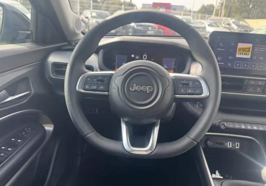 Vue intérieure centrée sur le volant Jeep d'un Avenger gris foncé 2025 avec tableau de bord numérique et écran tactile.