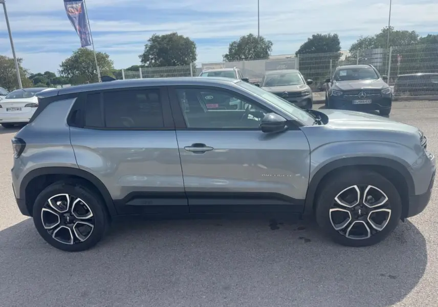 Vue de profil côté gauche d’un Jeep Avenger gris foncé 2025 avec jantes distinctives et toit noir contrasté.