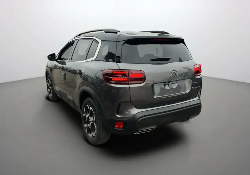 Vue 3/4 arrière d'un Citroën C5 Aircross 2025 gris platinium avec toit noir et feux arrière allumés.