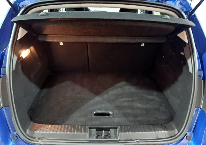Coffre ouvert vu de l'arrière d'un Renault Captur bleu 2023, avec plancher plat et éclairage intérieur à gauche.