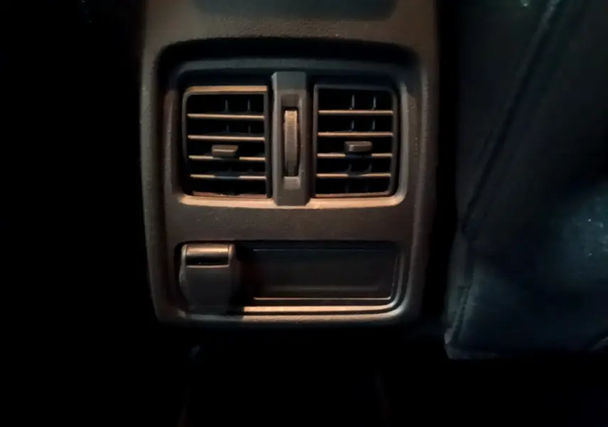 Gros plan sur la sortie d'air arrière et prise 12V noire dans l'habitacle du Renault Captur bleu 2023.