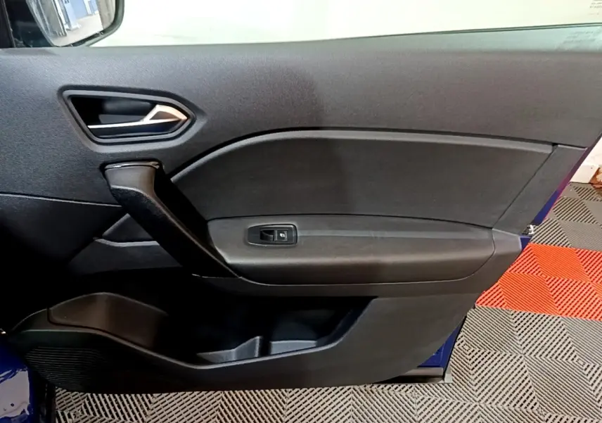 Vue intérieure du panneau de porte côté conducteur du Renault Captur bleu 2023, avec poignée noire et commande de vitre.