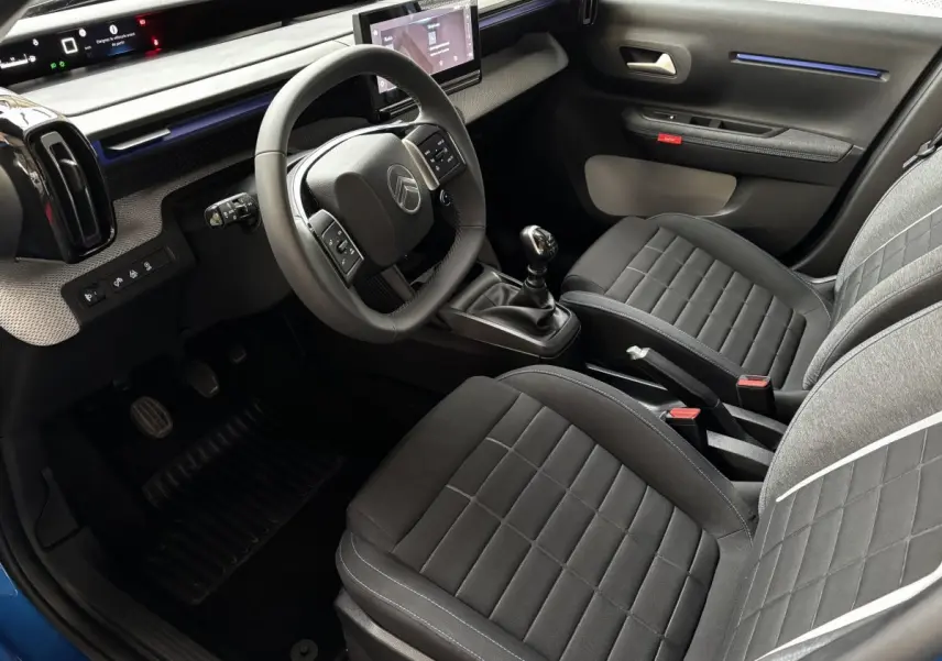 Vue intérieure côté conducteur de la Citroën C3 2025, volant cuir, sièges tissu noir et écran tactile central.