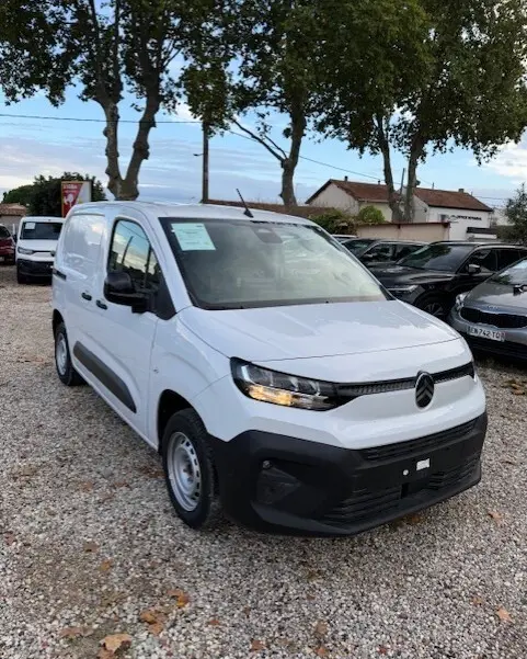 Citroën Berlingo Van blanc vu en 3/4 avant droit sur un parking, avec calandre noire et feux allumés.