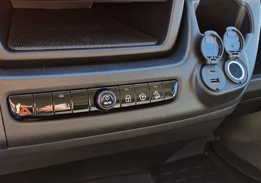 Détail de la console centrale noire du Fiat Ducato Chassis Benne 2023 avec boutons de contrôle et prises USB ouvertes.