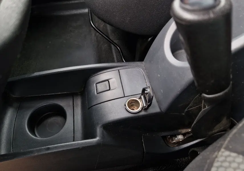Vue rapprochée de la console centrale noire du Renault Kangoo 2020, avec prise allume-cigare ouverte et frein à main visible.