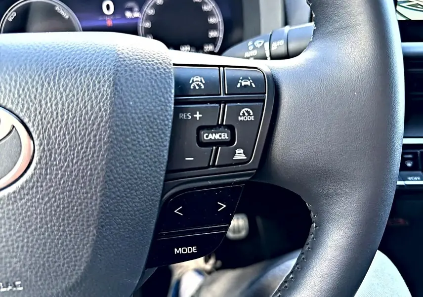 Gros plan sur le volant multifonction noir du Toyota C-HR 1.8 hybride 2025 avec commandes de régulateur et assistance.
