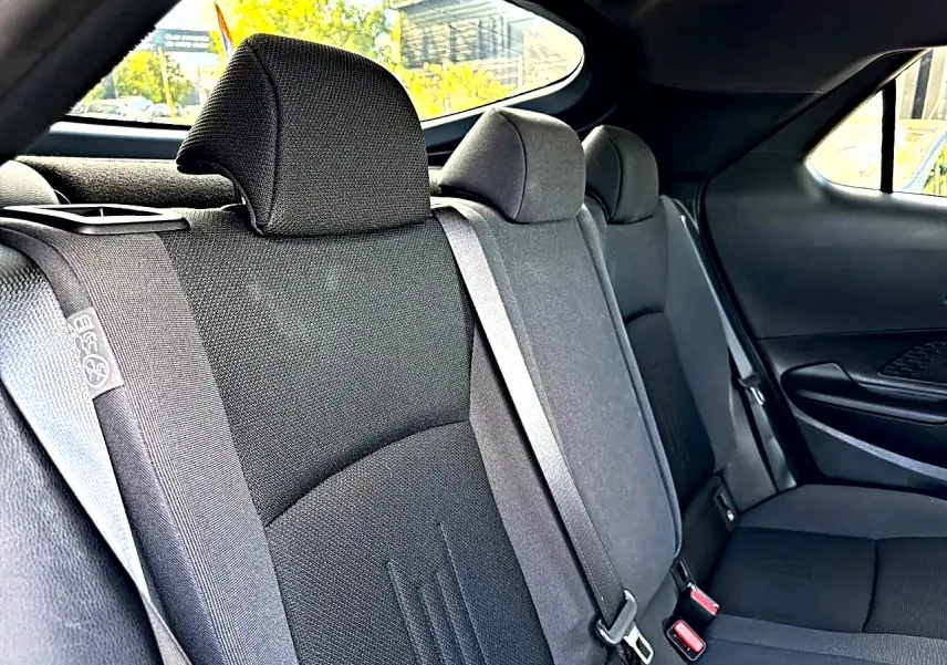 Vue intérieure arrière du Toyota C-HR 1.8 hybride 2025, montrant les sièges tissu gris foncé et les ceintures de sécurité.
