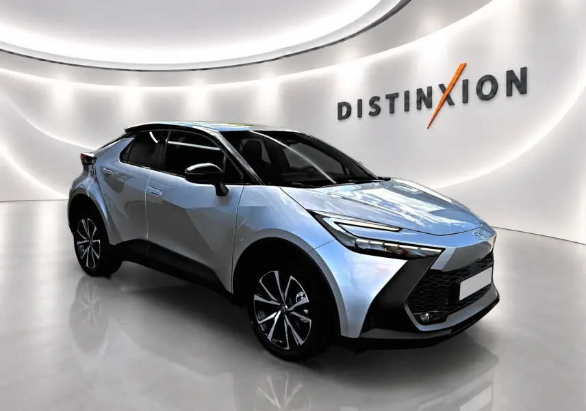 Toyota C-HR 1.8 hybride gris en 3/4 avant droit, avec jantes alliage et toit noir brillant dans un showroom lumineux.