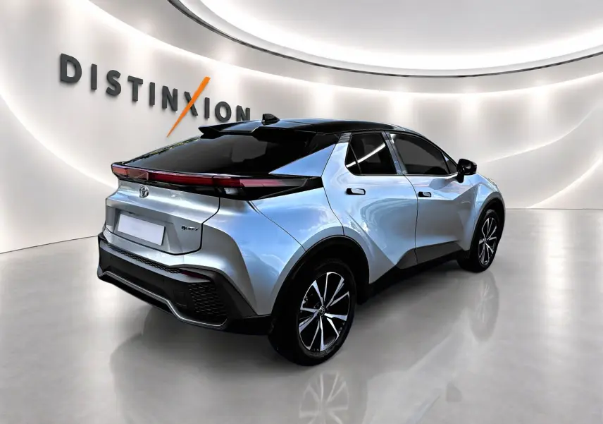 Toyota C-HR hybride gris 3/4 arrière droit, toit noir et jantes alliage dans un showroom lumineux.