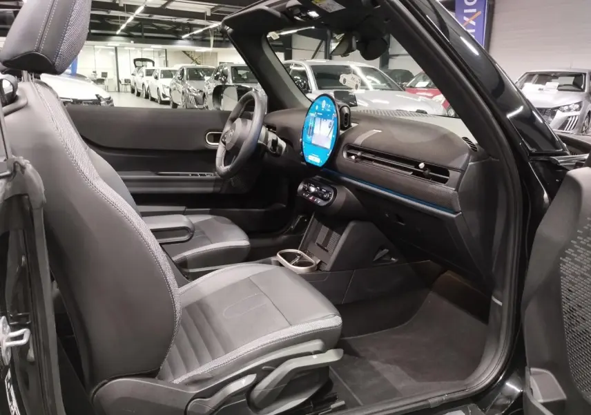 Vue intérieure côté passager d'une MINI Cabriolet noire 2025 avec tableau de bord moderne et sièges similicuir perforé.