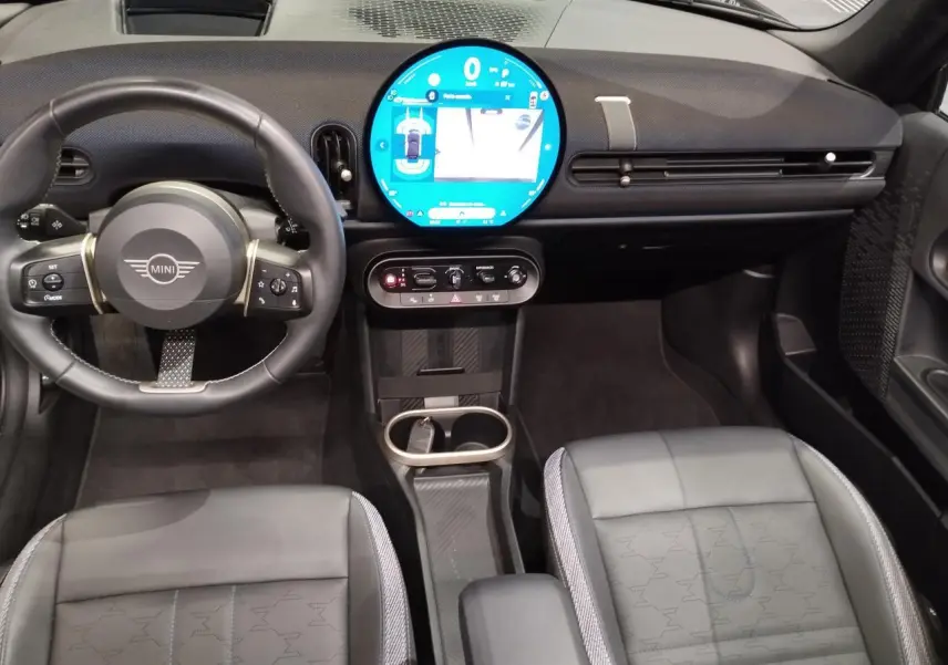 Intérieur avant noir du MINI Cabriolet 2025, vue centrée sur le volant et l'écran tactile circulaire lumineux.