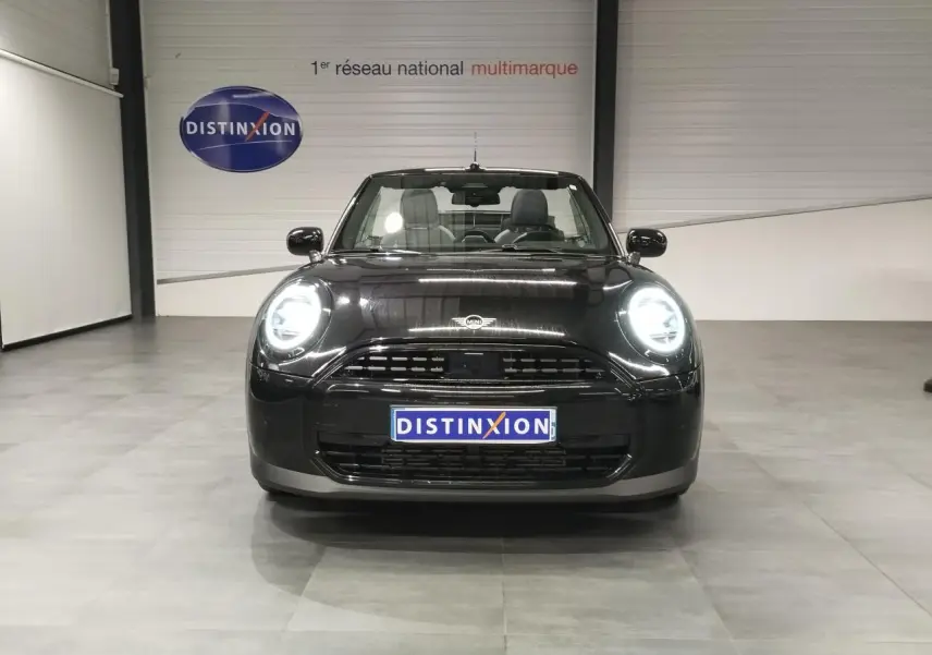 Vue avant d'une MINI Cabriolet noire 2025 avec phares LED allumés dans un showroom.
