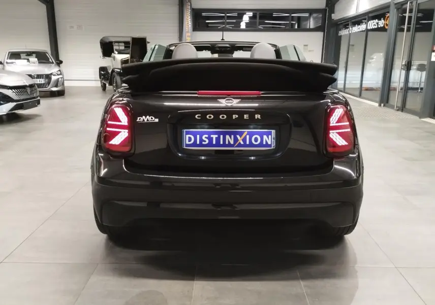 Vue arrière d'une MINI Cooper Cabriolet noire 2025 avec feux arrière LED en motif Union Jack et capote repliée.