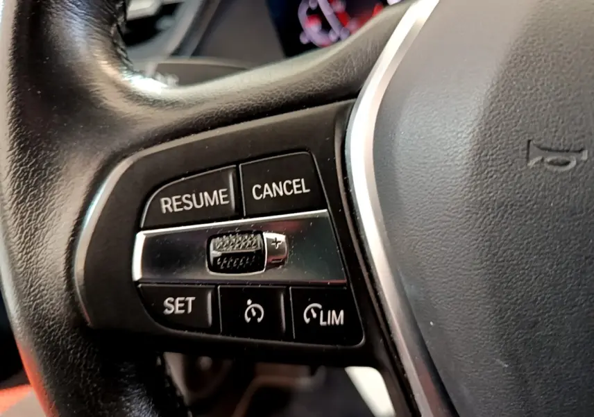 Gros plan sur les commandes de régulateur de vitesse au volant cuir noir d'une BMW Série 1 118i Edition Sport 2023.