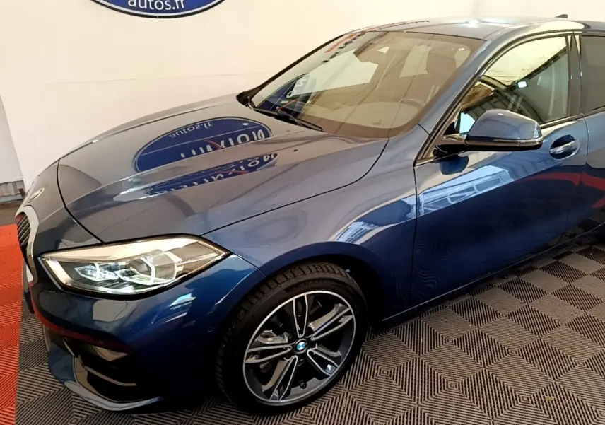 BMW Série 1 118i Edition Sport bleu vue 3/4 avant droit, avec phares LED et jantes alliage distinctives.