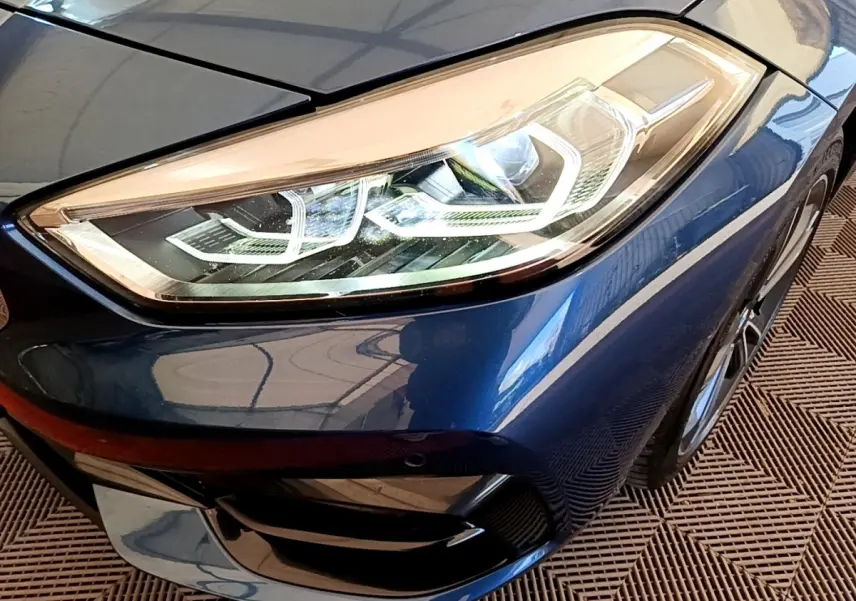 Gros plan sur le phare avant droit bleu d’une BMW Série 1 118i Edition Sport 2023 avec détails LED distinctifs.
