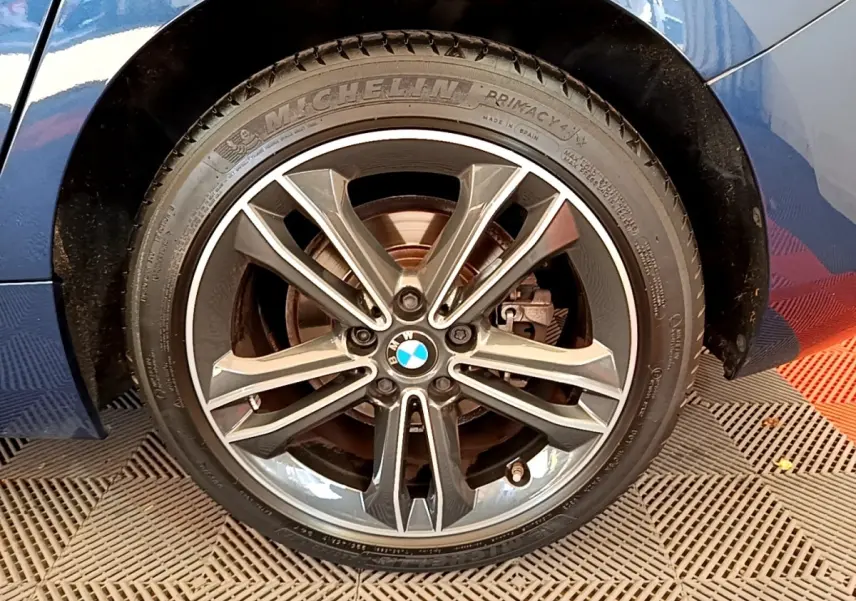 Gros plan sur la roue avant droite d’une BMW Série 1 118i bleu avec jante alliage et pneu Michelin.