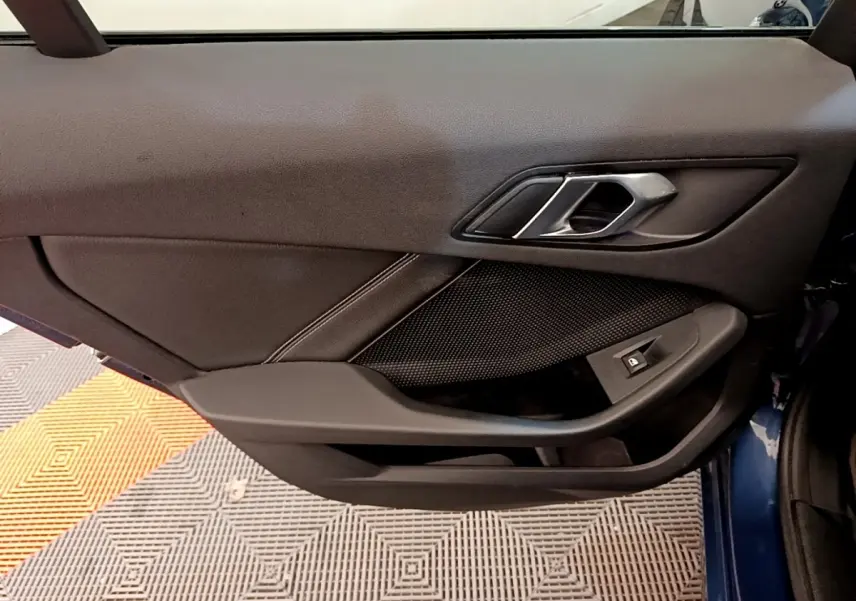 Gros plan sur la porte intérieure côté gauche d'une BMW Série 1 118i Edition Sport bleu, avec poignée et commande de vitre.