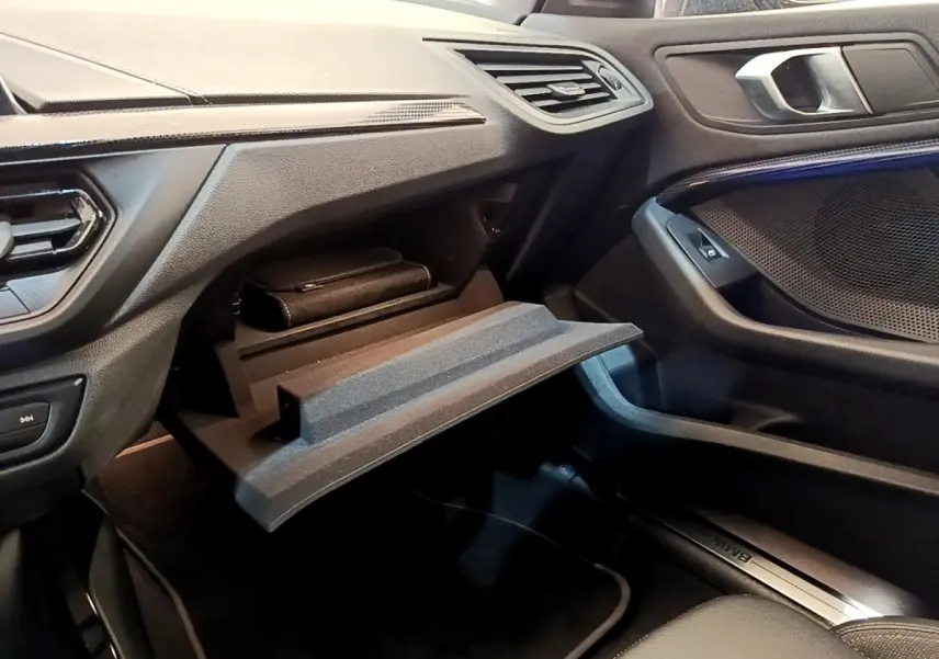 Intérieur BMW Série 1 118i Edition Sport 2023, vue côté passager sur boîte à gants ouverte et tableau de bord noir.
