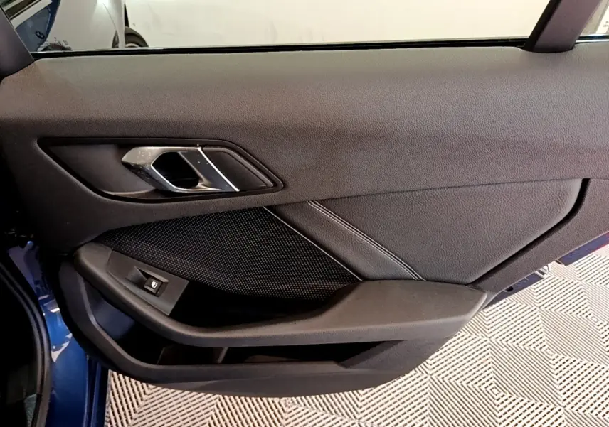 Vue rapprochée de la porte côté gauche bleu de la BMW Série 1 118i Edition Sport avec poignée et bouton de vitre électrique.