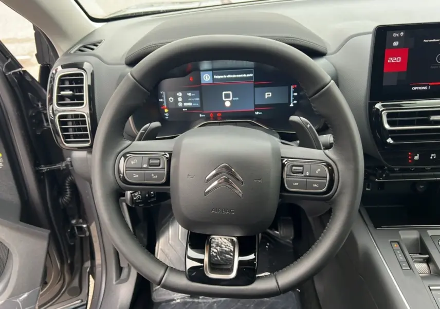 Vue intérieure centrée sur le volant du Citroën C5 Aircross Hybrid 2025 avec tableau de bord numérique et commandes intégrées.