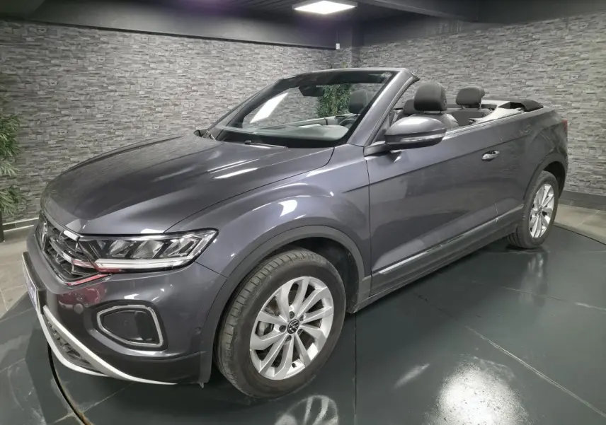 Volkswagen T-Roc cabriolet gris métallisé vu de 3/4 avant droit avec capote ouverte en intérieur showroom.