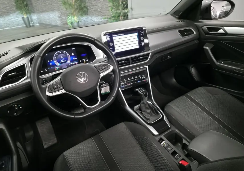 Intérieur avant du Volkswagen T-Roc gris 2024, volant cuir multifonction et écran tactile central visible.