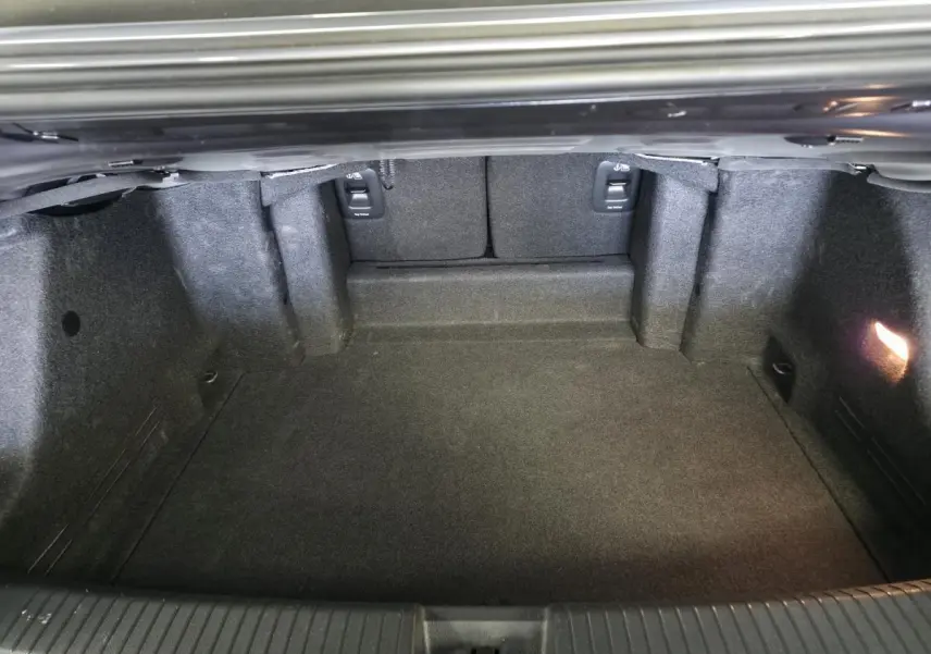 Coffre ouvert vu de l'arrière du Volkswagen T-Roc gris 2024, montrant un espace de chargement propre et éclairé.