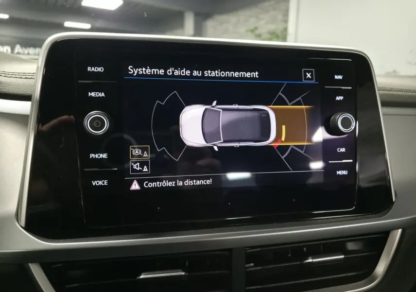 Écran central du Volkswagen T-Roc 2024 affichant l'aide au stationnement avec vue du dessus du véhicule gris.