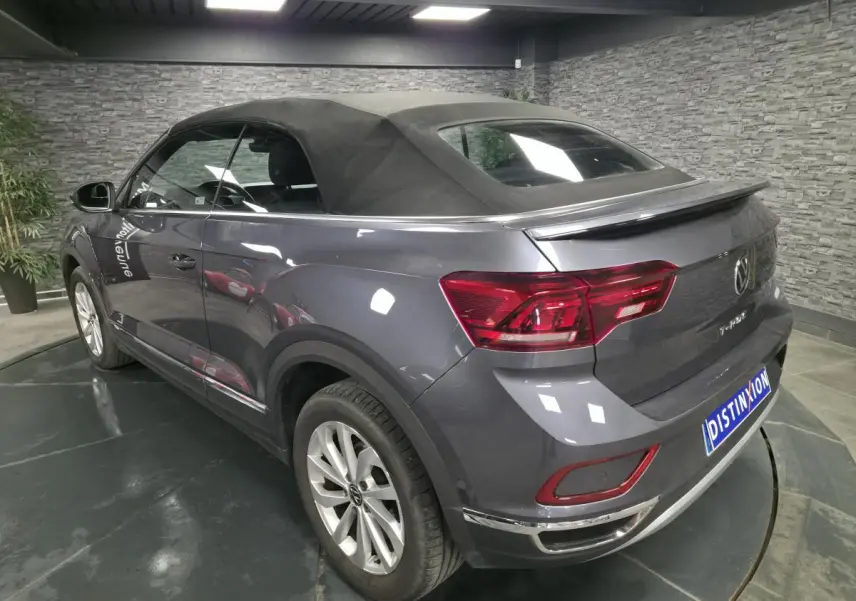 Vue 3/4 arrière droite du Volkswagen T-Roc gris métallisé avec capote noire en intérieur showroom.