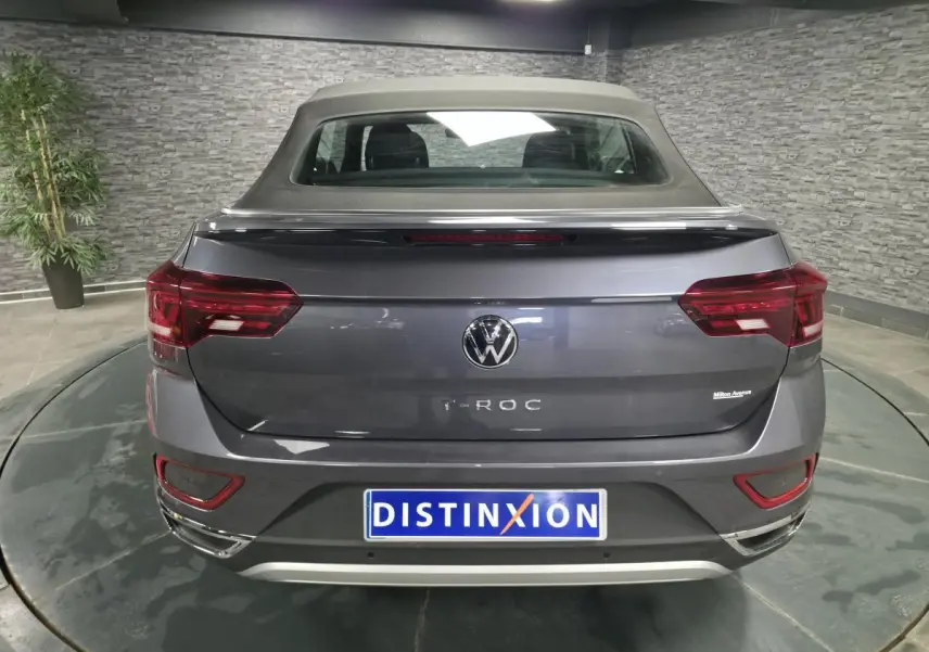 Vue arrière d'un Volkswagen T-Roc gris métallisé avec capote noire en textile dans un showroom.