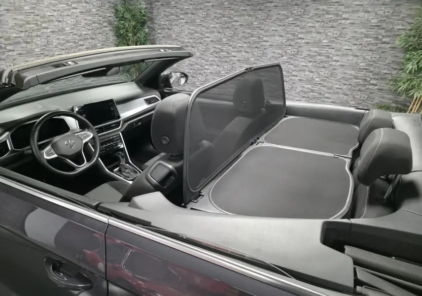 Vue intérieure côté conducteur d'un Volkswagen T-Roc cabriolet gris avec volant multifonction et capote ouverte.