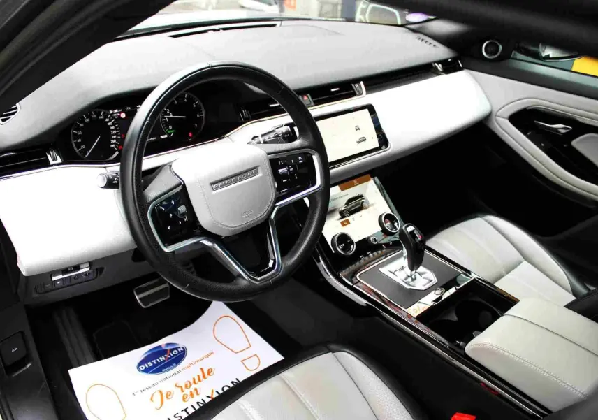Intérieur clair du Range Rover Evoque 2023, vue côté conducteur, volant multifonction et écran tactile central.